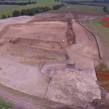 A view of the site with one of the wetland areas surrounded by orange fencing in the foreground and our team excavating to the left of the white van. Can you spot the two enclosures in the top left of the photo?