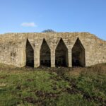In this week’s #BuildingKnowledge we take a quick look at the Grade II Listed Hartington Lime Kilns, Northumberland. This magnificent structure has been built from well-dressed squared and coursed sandstone blocks, and features four large triangular openings, which appear reminiscent of a lair from an epic fantasy film! These openings are corbelled down, with 2 oval brick-lined pots at their bases. In this week’s #BuildingKnowledge we take a quick look at the Grade II Listed Hartington Lime Kilns, Northumberland. This magnificent structure has been built from well-dressed squared and coursed sandstone blocks, and features four large triangular openings, which appear reminiscent of a lair from an epic fantasy film! These openings are corbelled down, with 2 oval brick-lined pots at their bases. The now disused lime kilns related to a lime quarry to the east, with the area also retaining a fantastic range of ridge and furrow. © ARS Ltd 2023