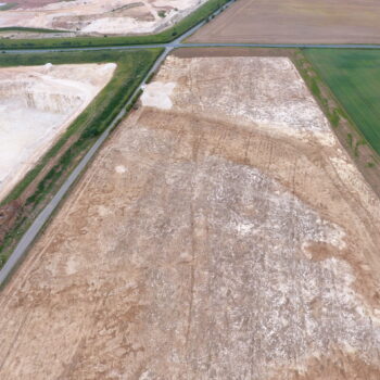 Aerial view of the south-east part of the site after top soil stripping in 2020. The ditches of the Late Iron Age to Roman north–south droveway can just be made out running down the centre of the field (from bottom to top), whilst the dark outline of a prehistoric palaeochannel/ palaeovalley runs across the field from north-west to south-east to (right to left) © ARS Ltd 2024